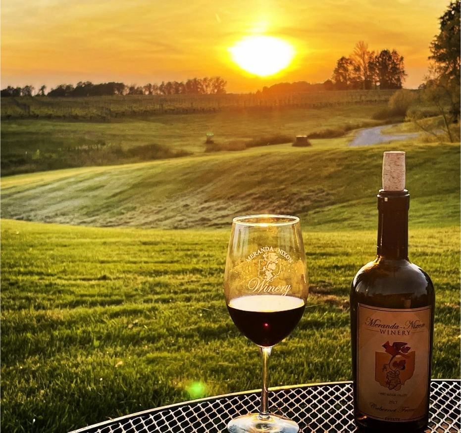 Wine bottle and glass at sunset vineyard.